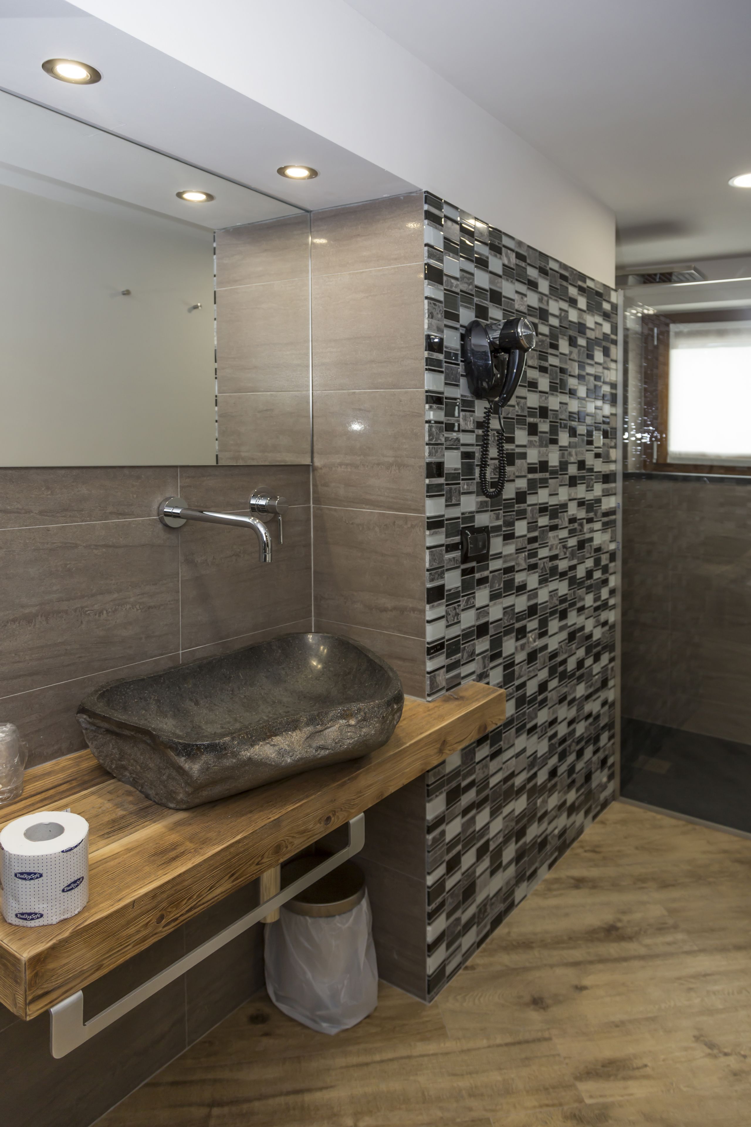A bathroom with a wooden vanity, a stone sink, and a tiled backsplash.