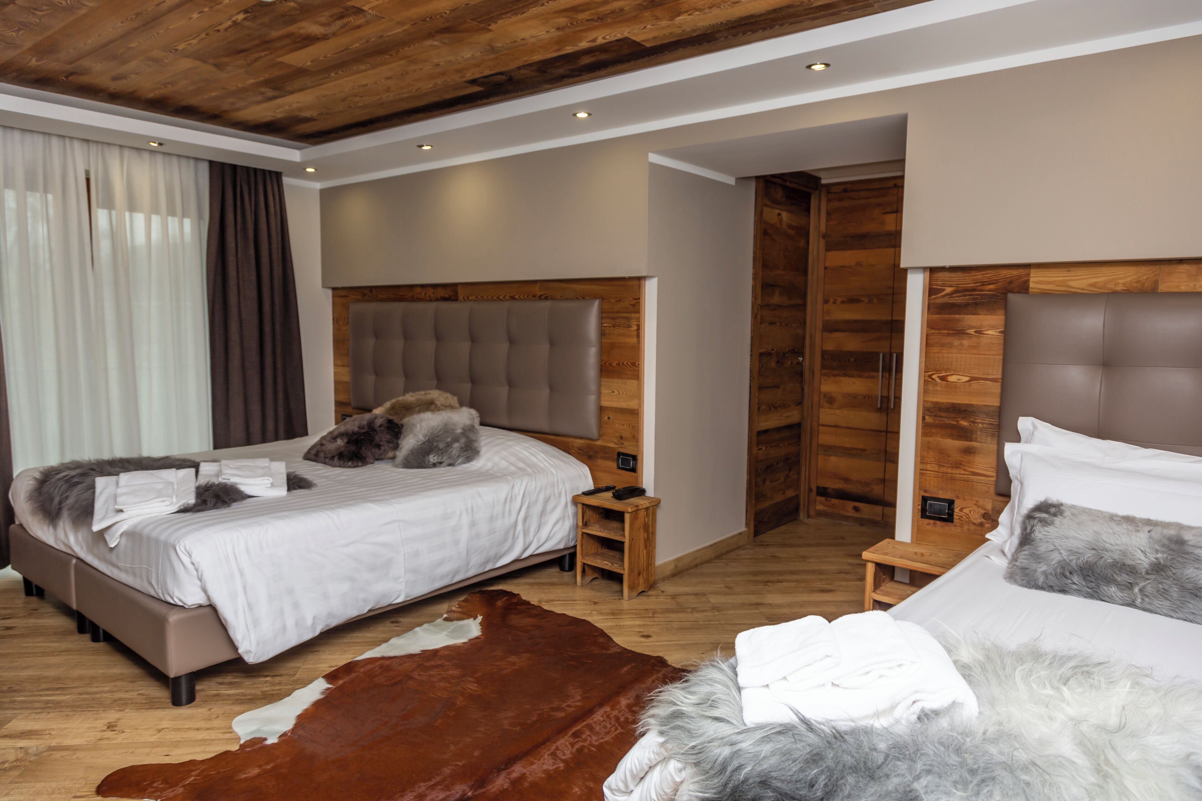 Ein modernes Schlafzimmer mit zwei Betten, Holz-Kopfteilen und einem Kuhfellteppich.