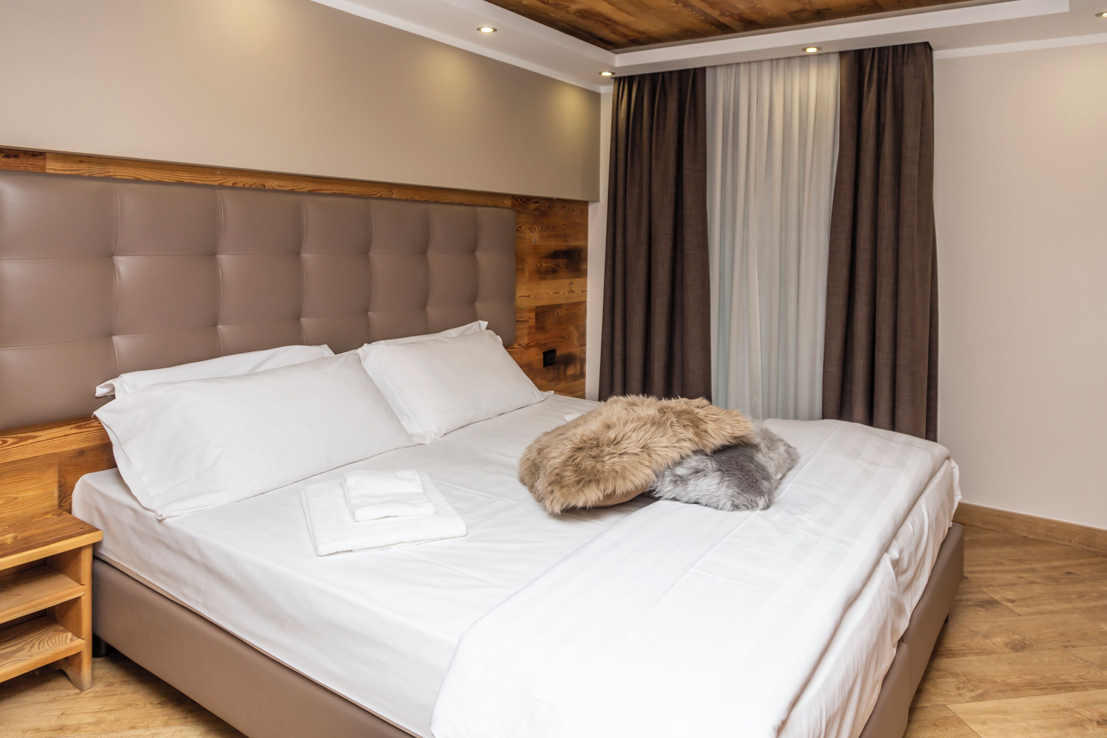 A neatly made bed with white linens and a fluffy pillow, a wooden headboard, and a wooden nightstand with a lamp.