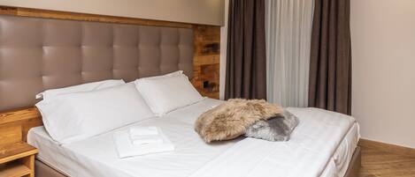 A neatly made bed with white linens and a fluffy pillow, a wooden headboard, and a wooden nightstand with a lamp.