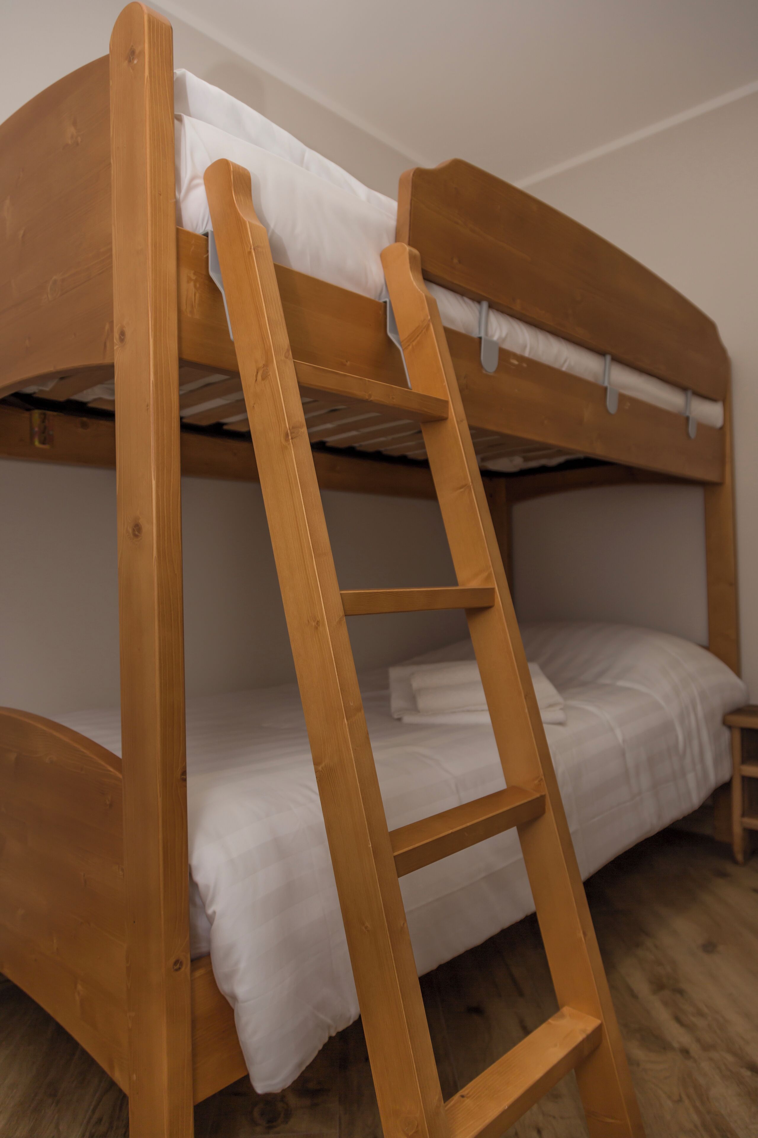 A bunk bed with a wooden ladder, white bedding, and a small wooden stool.