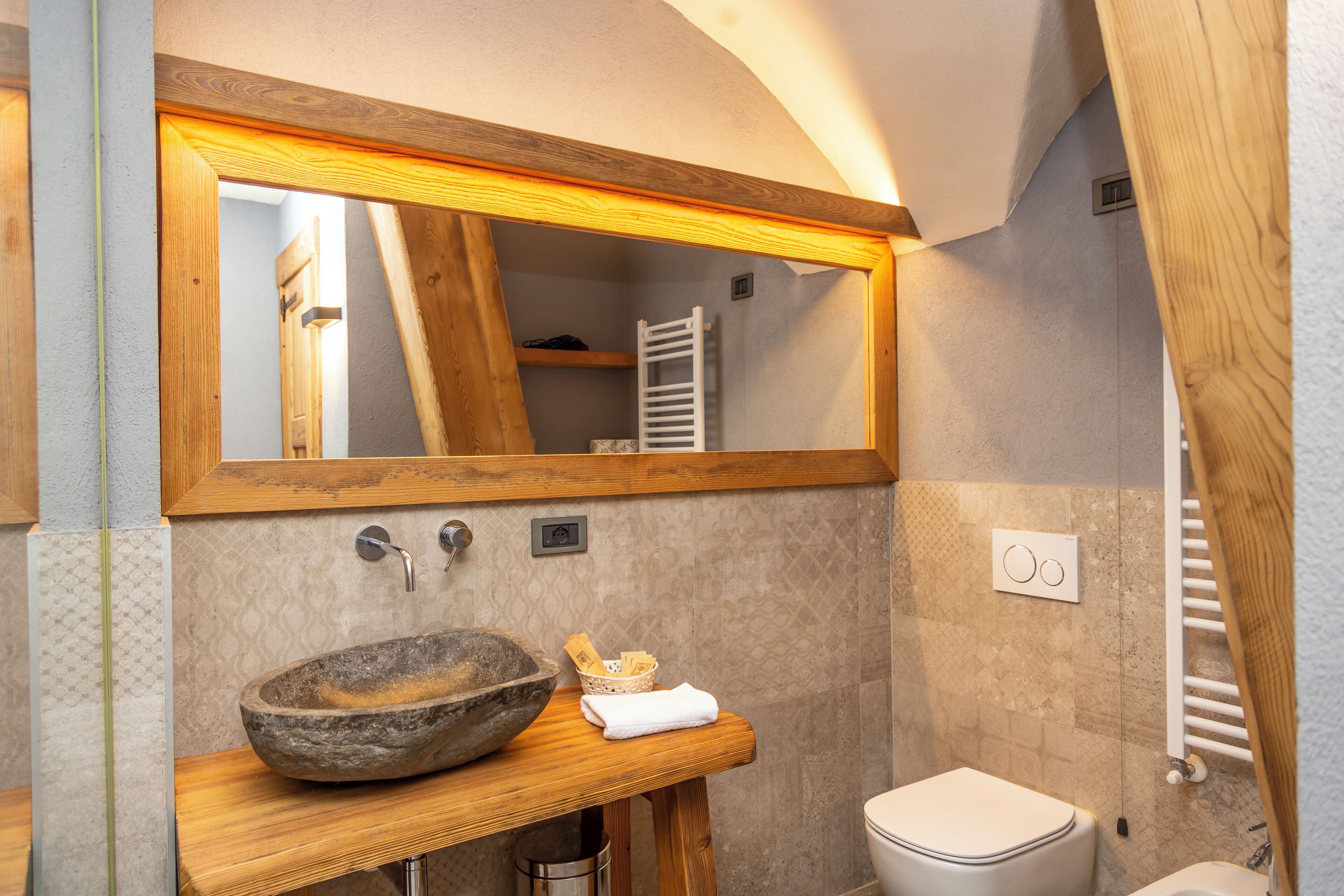 Une salle de bain avec un meuble-lavabo en bois, un grand miroir, un lavabo en pierre et des toilettes blanches.