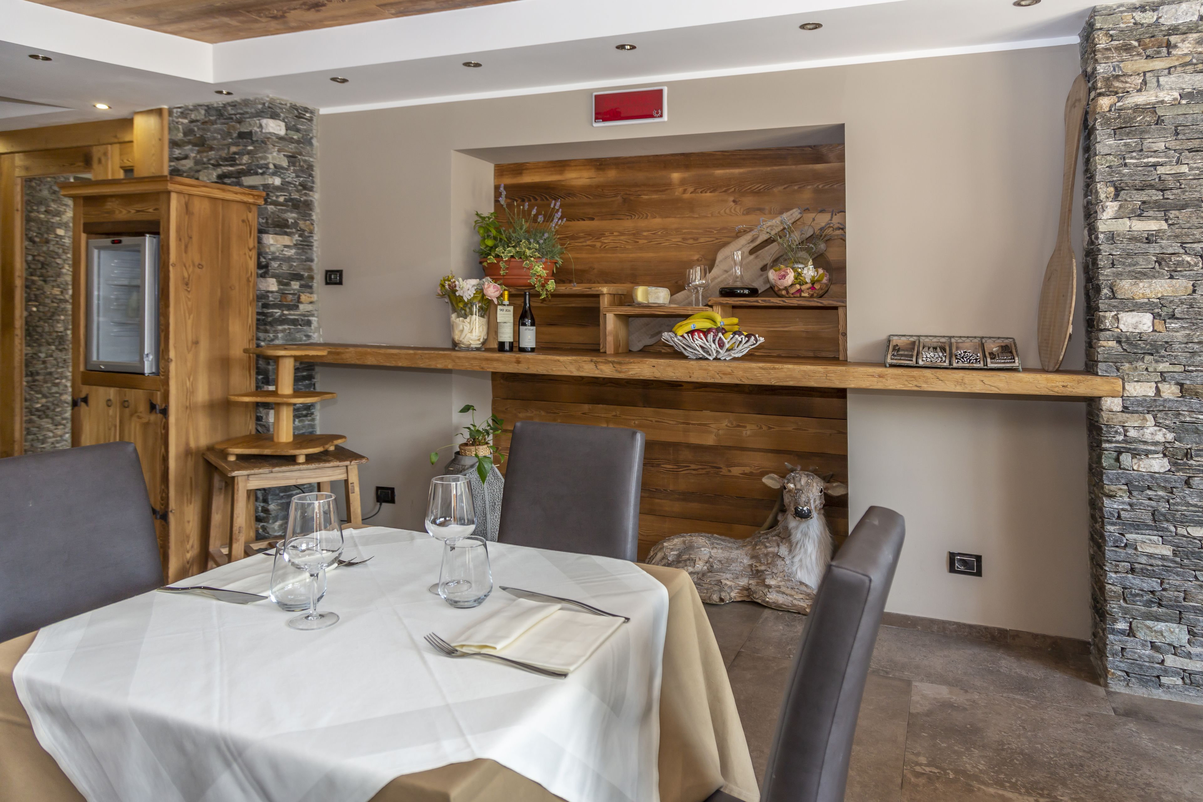 A dining area with a table set for two, a wooden cabinet, and a stone wall.