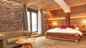 Una habitación acogedora con pared de piedra, cama de madera, sofá de cuero y una pequeña mesa de madera.