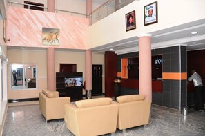 A hotel lobby with a reception desk, a TV, and a seating area with two sofas. - Georgetown Hotel (Abuja)