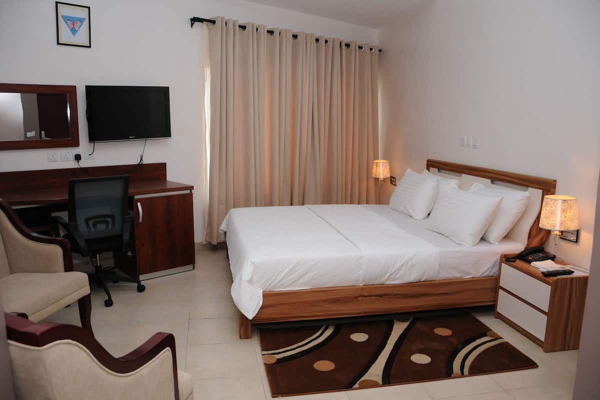 Una camera d'albergo con un letto, una scrivania, una sedia, una televisione e tende.