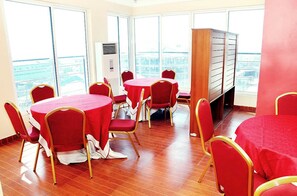 A conference room with round tables and red chairs, large windows with a city view, and a wooden cabinet. - Georgetown Hotel (Abuja)