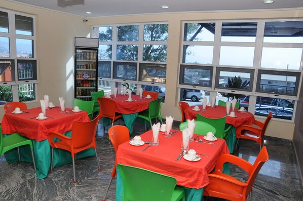 A dining area with tables set for service, large windows, and a refrigerator stocked with beverages. - Georgetown Hotel (Abuja)