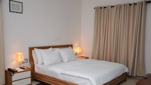 A neatly made bed with white linens and a wooden headboard, flanked by bedside tables with lamps and a phone.