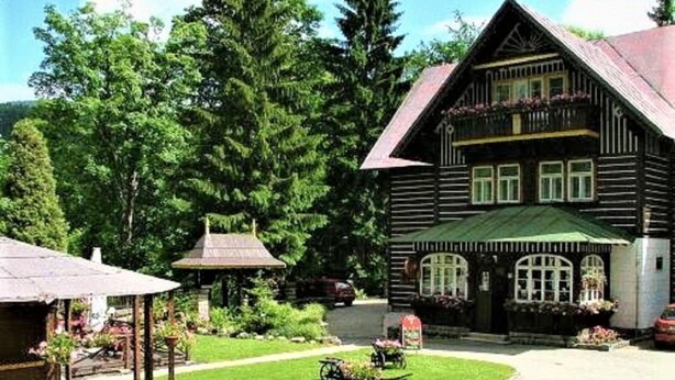 A wooden building with a green roof, surrounded by lush greenery and a small garden. - Hotel Tři růže (Spindleruv Mlyn)