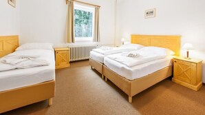 A hotel room with two beds, a radiator, a window with curtains, and a bedside table with a lamp. - Hotel Tři růže (Spindleruv Mlyn)