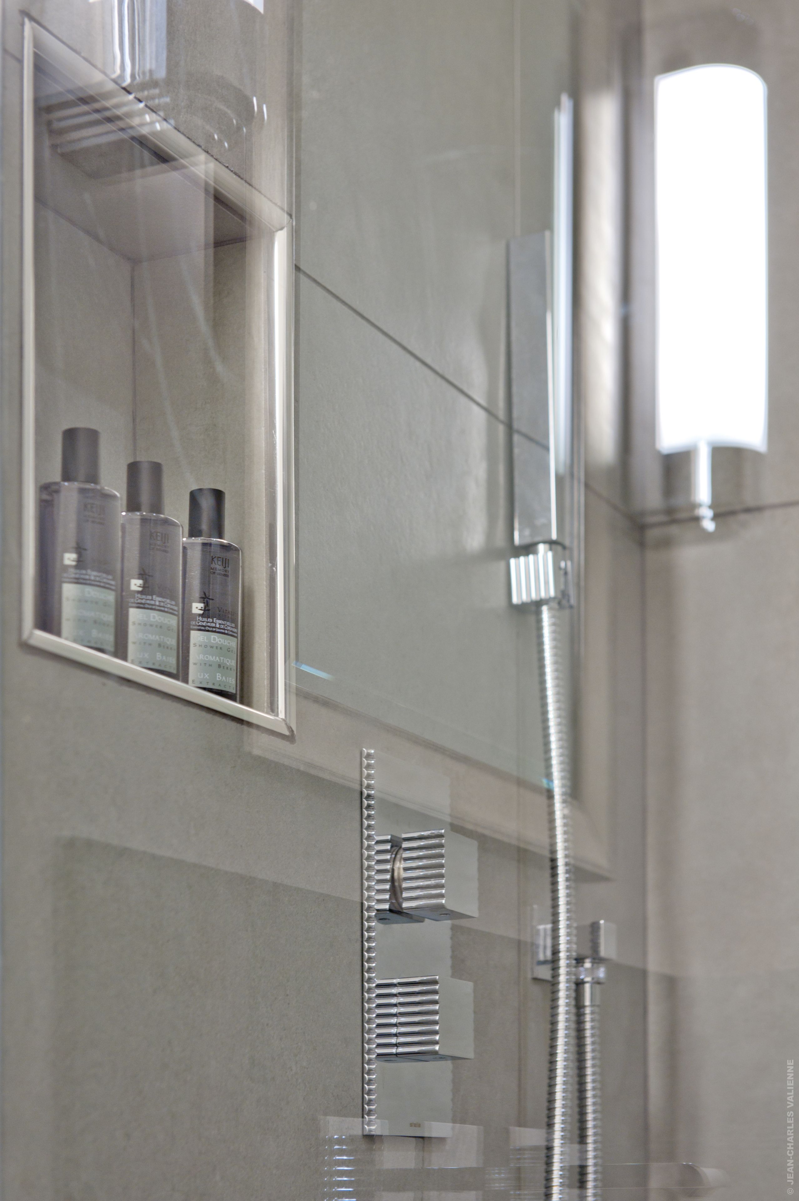 Une salle de bain avec une douche à parois de verre, un miroir et une étagère contenant des articles de toilette.