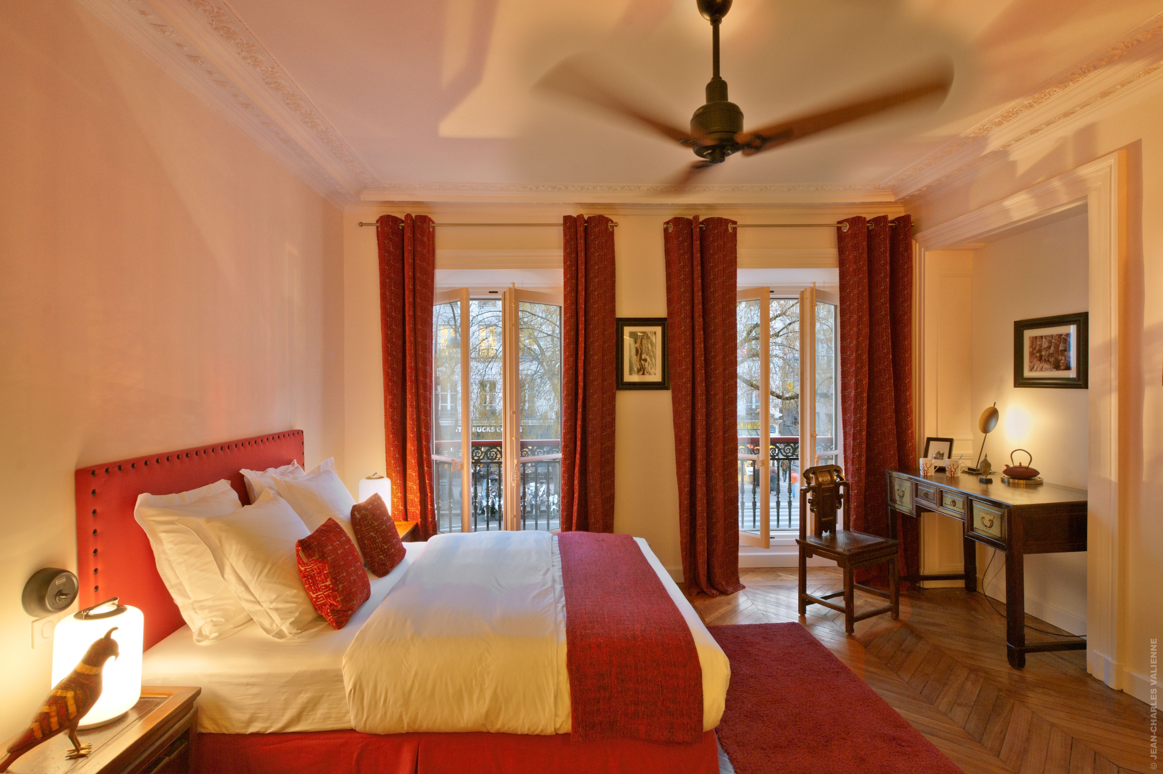 A hotel room with a bed, a desk, a chair, and a view of the outside through large windows.