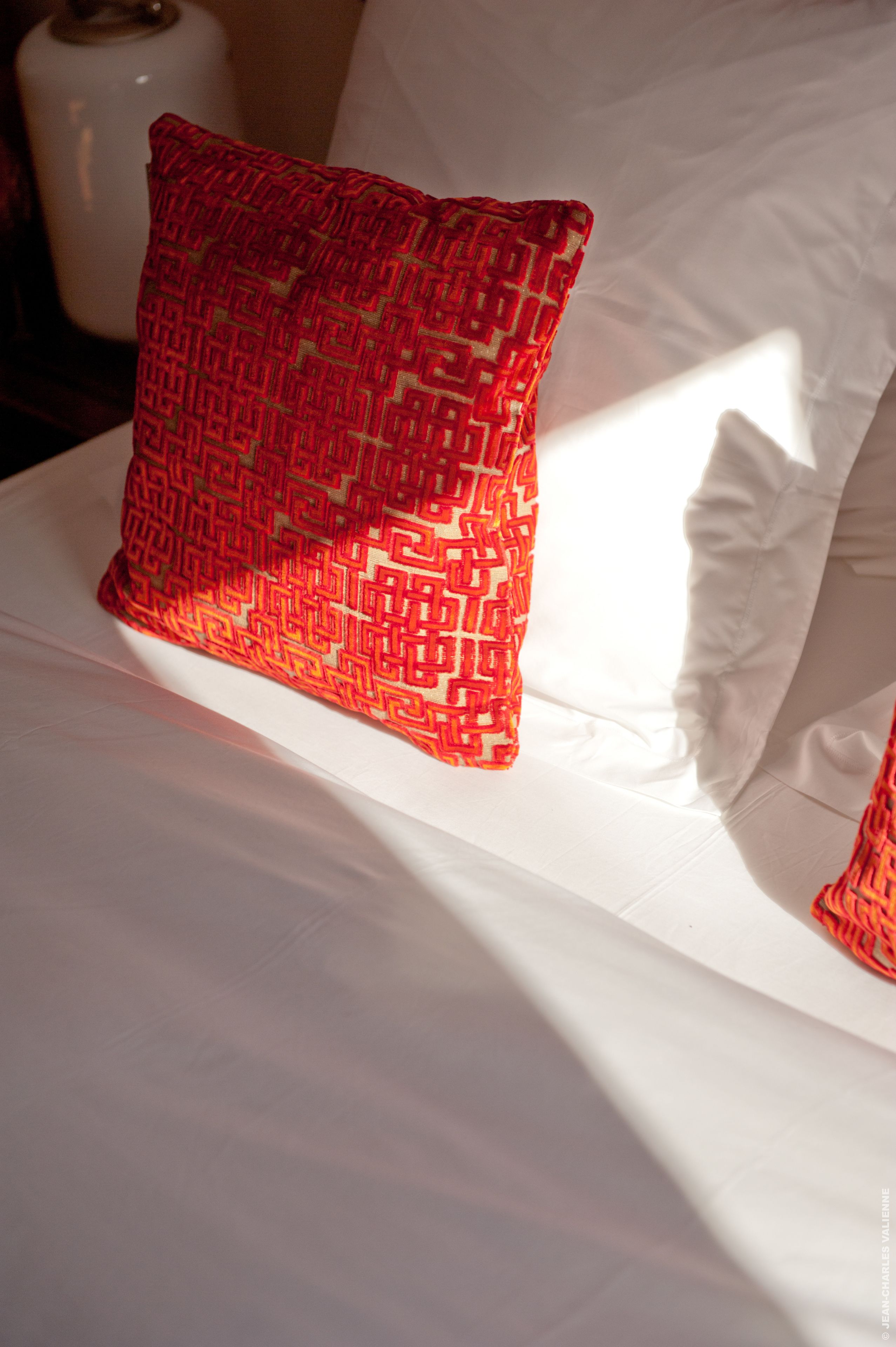 A bed with a white sheet and a red patterned pillow.