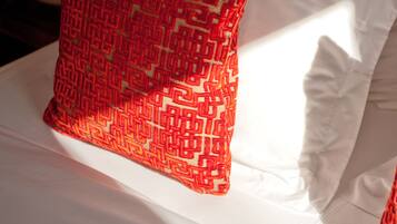 Una cama con sábana blanca y almohada de estampado rojo.
