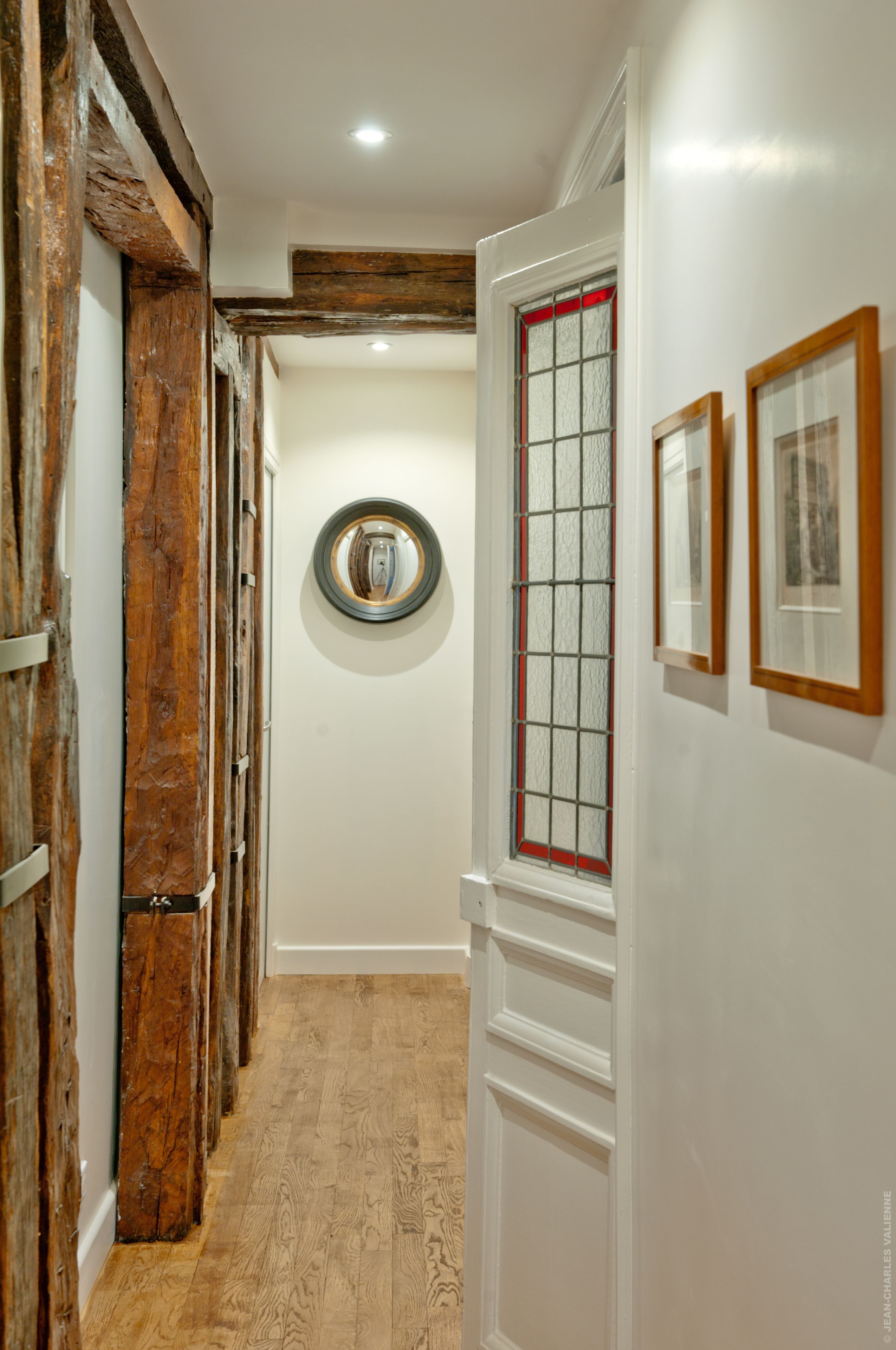 A hallway with wooden beams, a round mirror, and framed pictures on the wall.