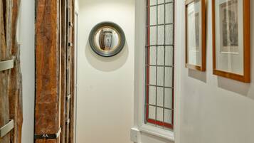 A hallway with wooden beams, a round mirror, and framed pictures on the wall.