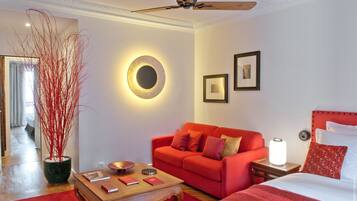 A hotel room with a red sofa, a wooden coffee table, a bed with a red headboard, a ceiling fan, and a wall-mounted circular light fixture.