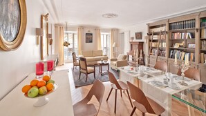 A spacious living room with a dining area, a large bookshelf, and a painting on the wall. - My Home For You B&B (Paris)