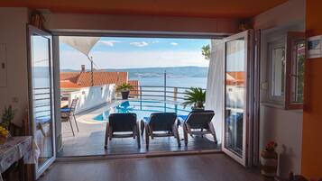 A balcony with a pool, two chairs, and a table with a potted plant.