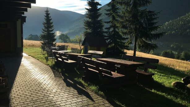 An outdoor seating area with picnic tables and benches, surrounded by trees and a mountainous landscape. - Hotel Výsluní (Spindleruv Mlyn)