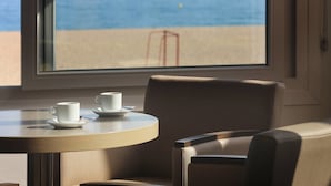 Una habitación con vista a la playa, una mesa redonda con dos tazas blancas y una sola silla.