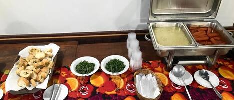 A buffet table with various food items, including a dish with meat, bowls of green vegetables, and a container of ice.