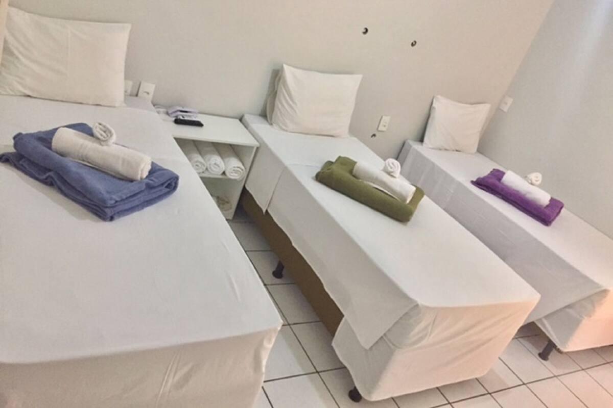 Habitación de hotel con tres camas, cada una con colchón y almohadas blancos. Toallas de varios colores sobre cada cama.
