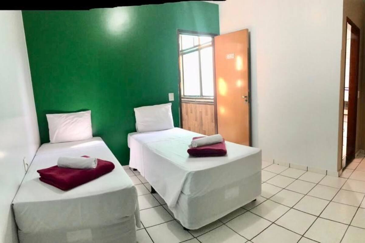 Habitación de hotel con dos camas, una pared de acento verde, una ventana y una puerta que da a otra habitación.
