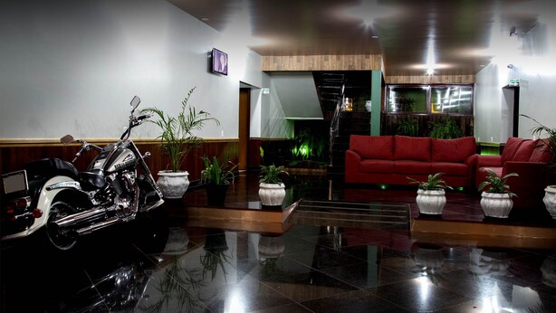 A lobby with a motorcycle, red sofas, and potted plants. - Acapú Hotel (Rio Verde)