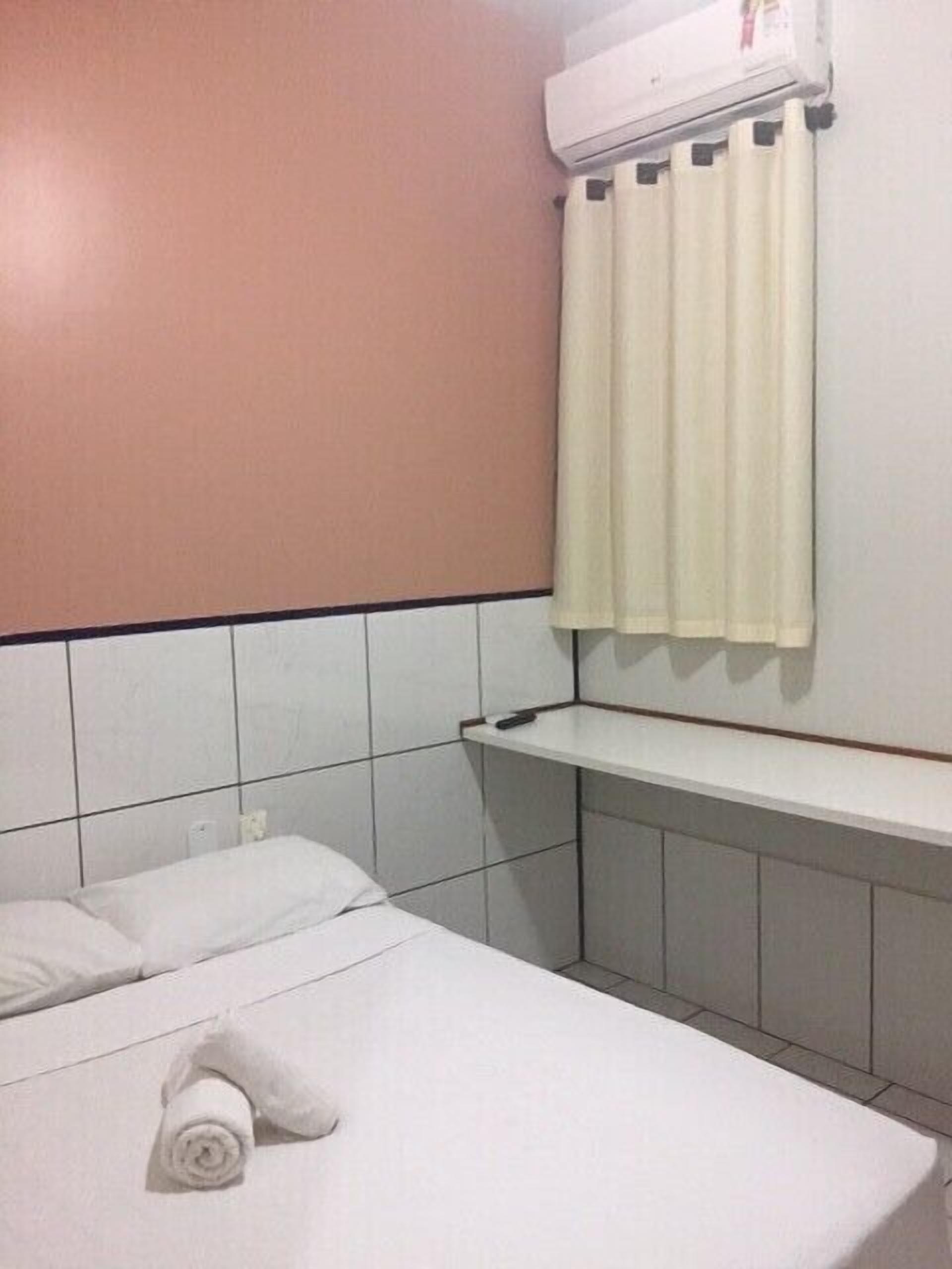 A hotel room with a bed, a white towel, a shelf, and an air conditioning unit.