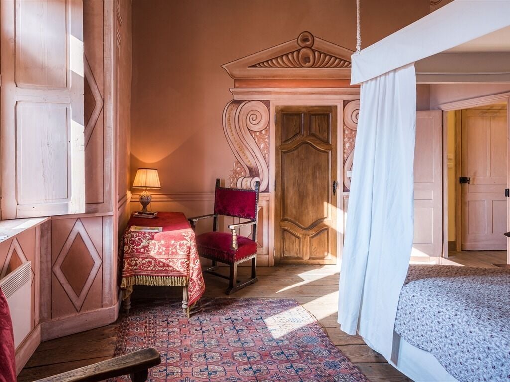Una habitación con un rug adornado, una puerta de madera, una silla roja y una cama con dosel blanco.