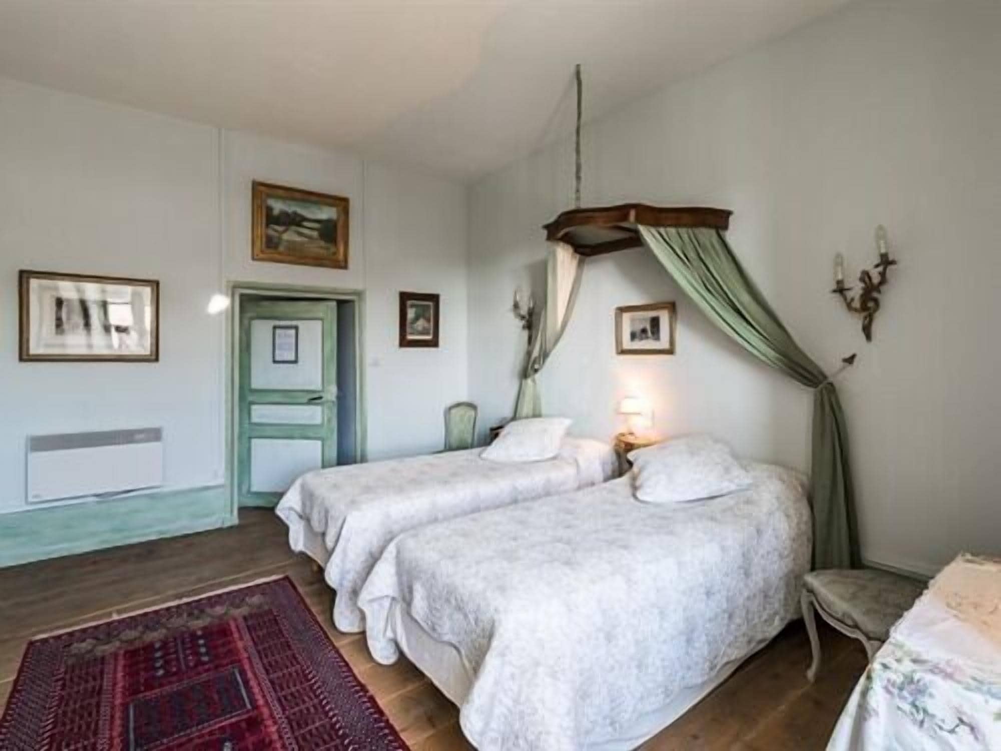 A bedroom with two beds, a wooden floor, a red rug, and a green door.
