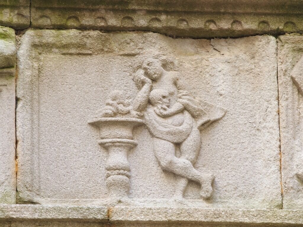 Una escultura de pedra d'una figura asseguda sobre un pedestal.