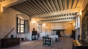 Una habitación amplia con techo alto, vigas de madera, chimenea y una mesa de comedor con sillas.