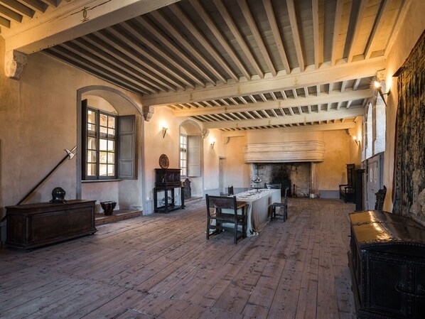 A spacious room with a high ceiling, wooden beams, a fireplace, and a dining table with chairs.