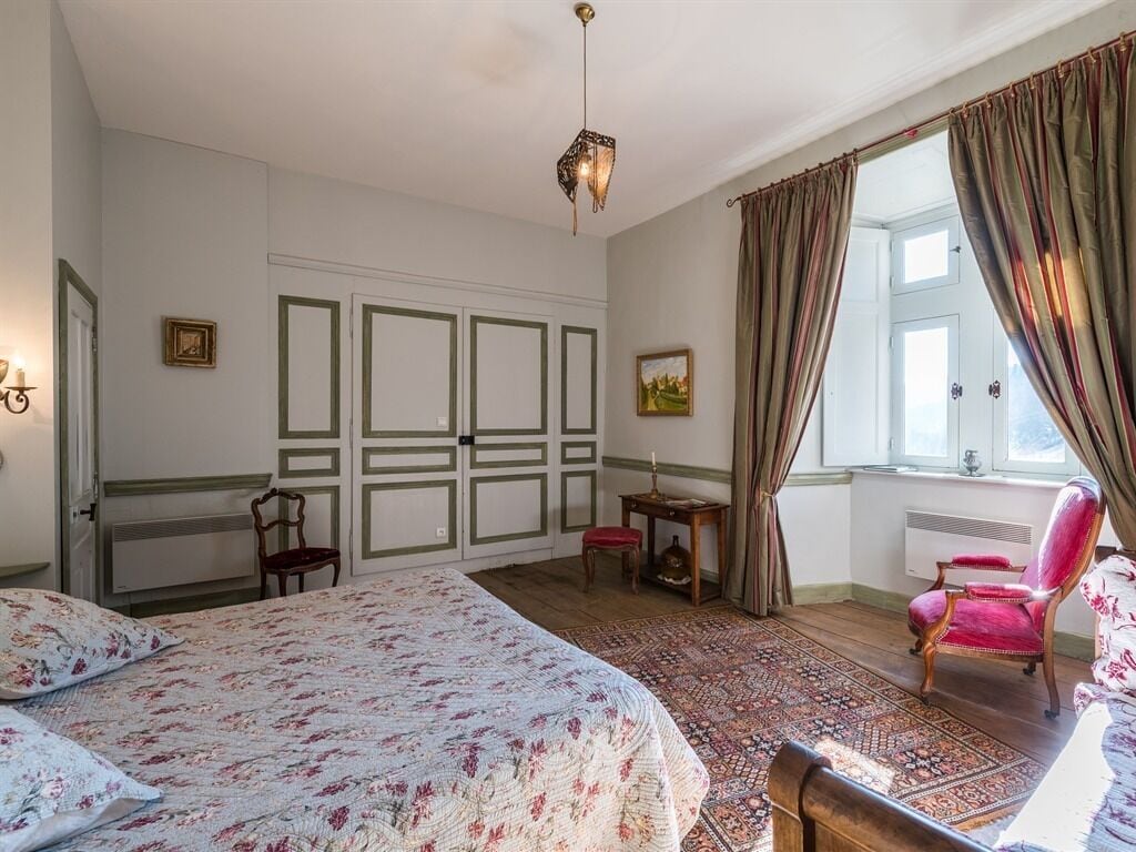 Ein Schlafzimmer mit einem großen Bett, einem Sessel, einem kleinen Tisch und einem Fenster mit Vorhängen.
