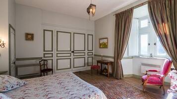 Ein Schlafzimmer mit einem großen Bett, einem Sessel, einem kleinen Tisch und einem Fenster mit Vorhängen.