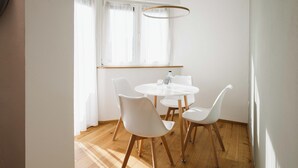 Un comedor con una mesa redonda, cuatro sillas blancas, una lámpara colgante y una ventana con cortinas de gasa.