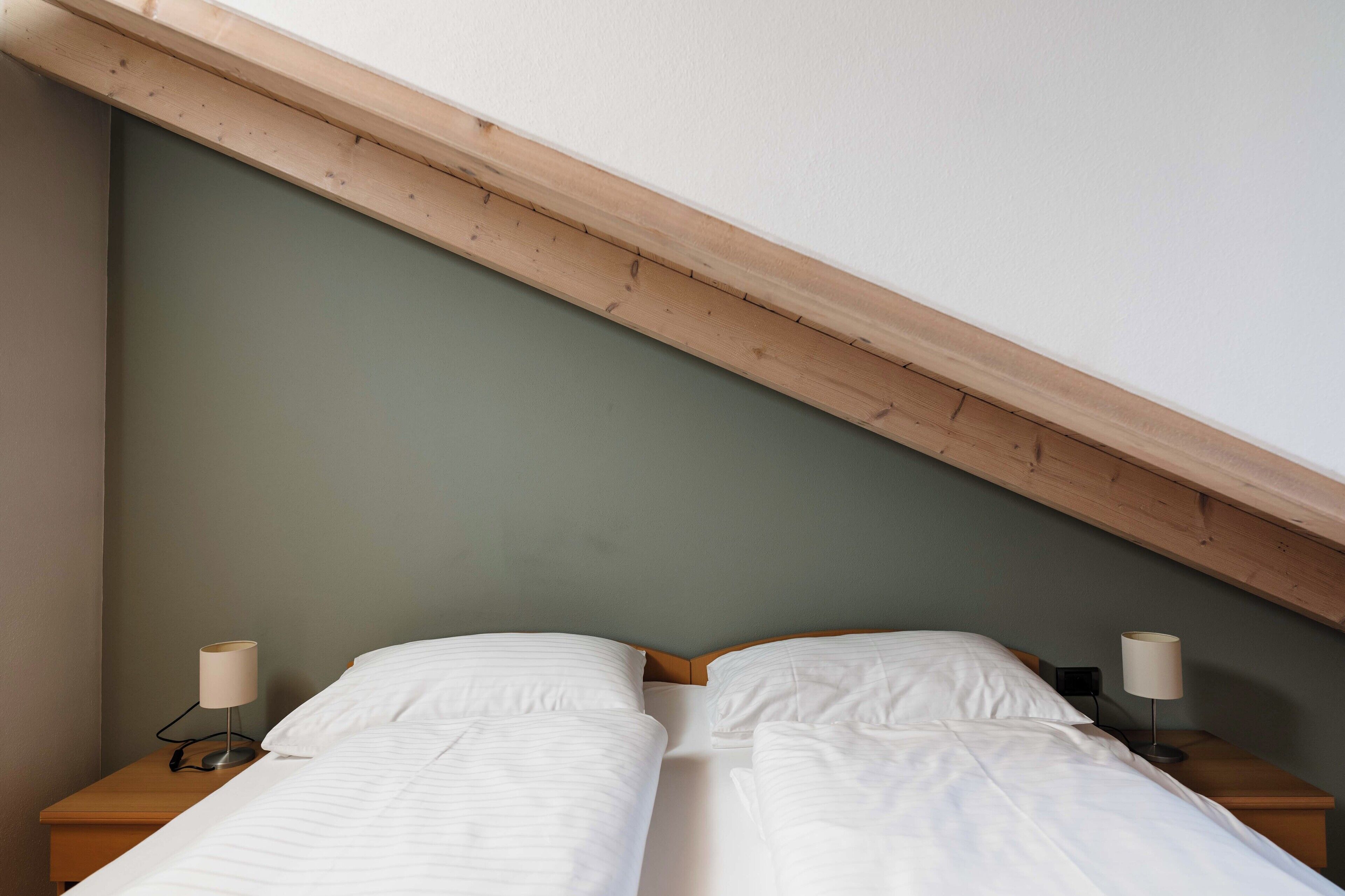 Ein Schlafzimmer mit zwei Einzelbetten, Holz-Kopfteilen und Nachttischlampen.
