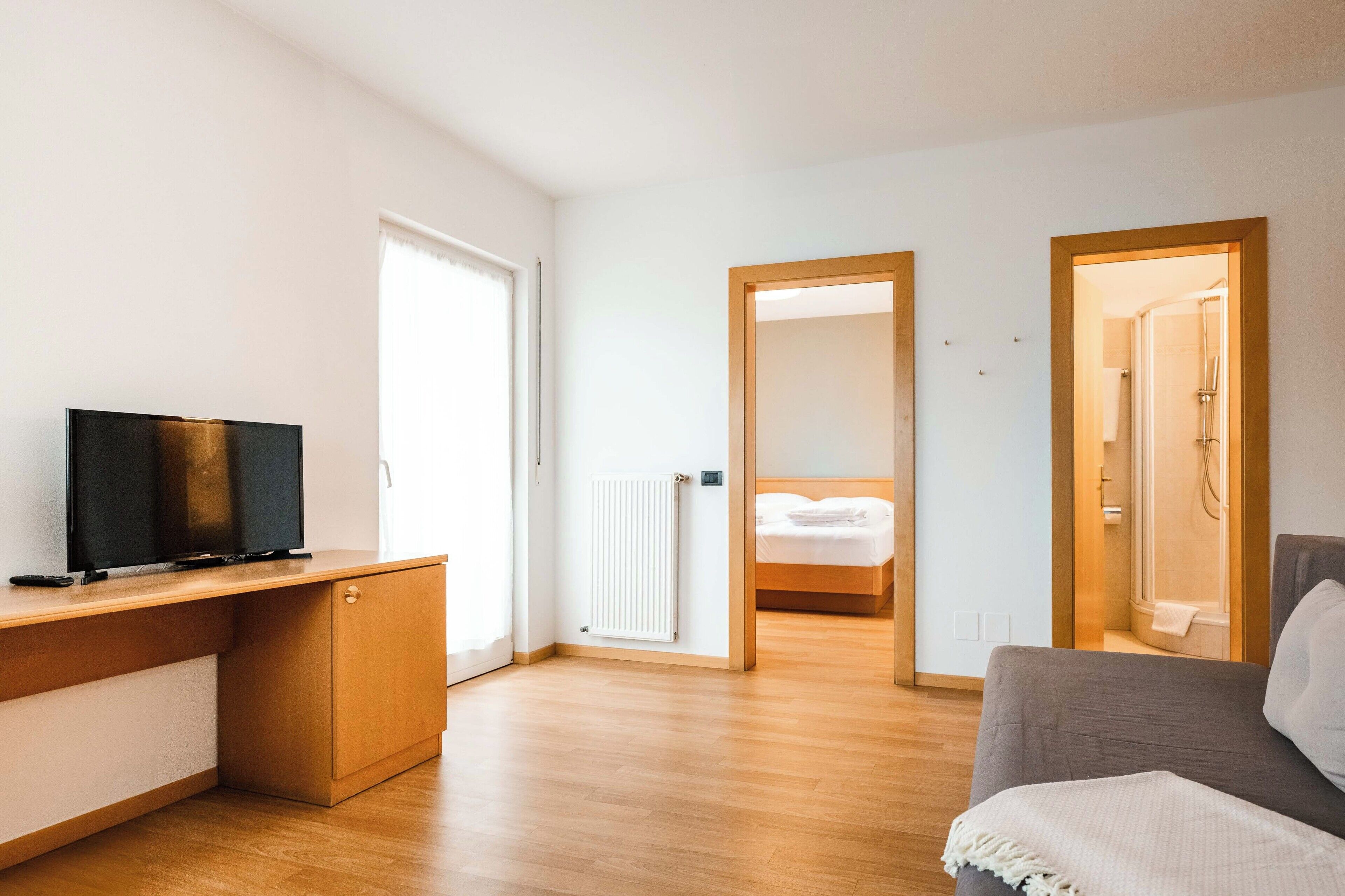 A modern room with a wooden desk, a television, a grey sofa, and a bed with a wooden headboard.