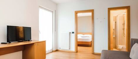 A modern room with a wooden desk, a television, a grey sofa, and a bed with a wooden headboard.
