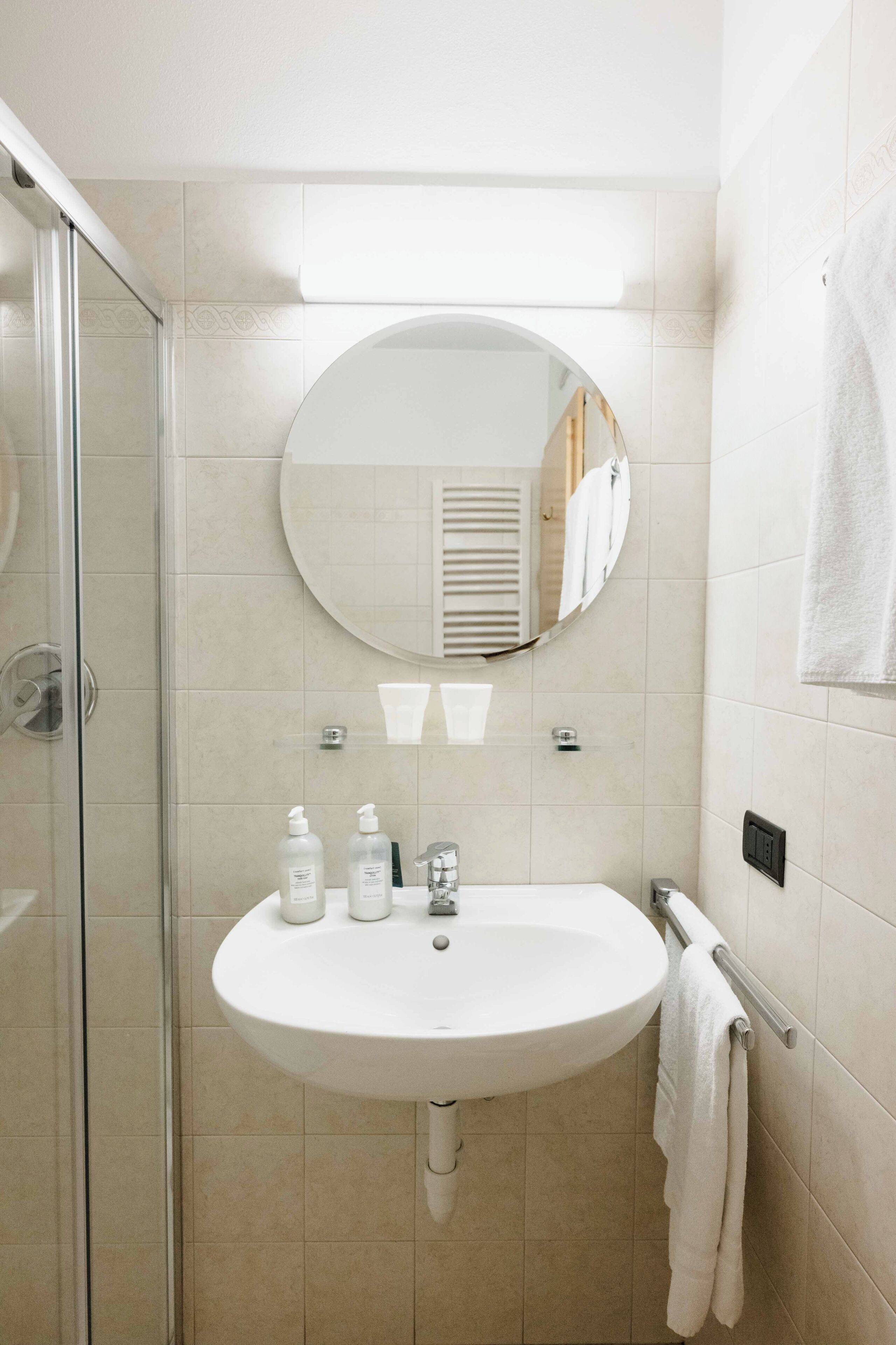 Une salle de bain avec une douche à parois de verre, un lavabo blanc avec un miroir au-dessus et un porte-serviettes.