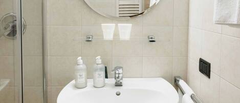 Une salle de bain avec une douche à parois de verre, un lavabo blanc avec un miroir au-dessus et un porte-serviettes.
