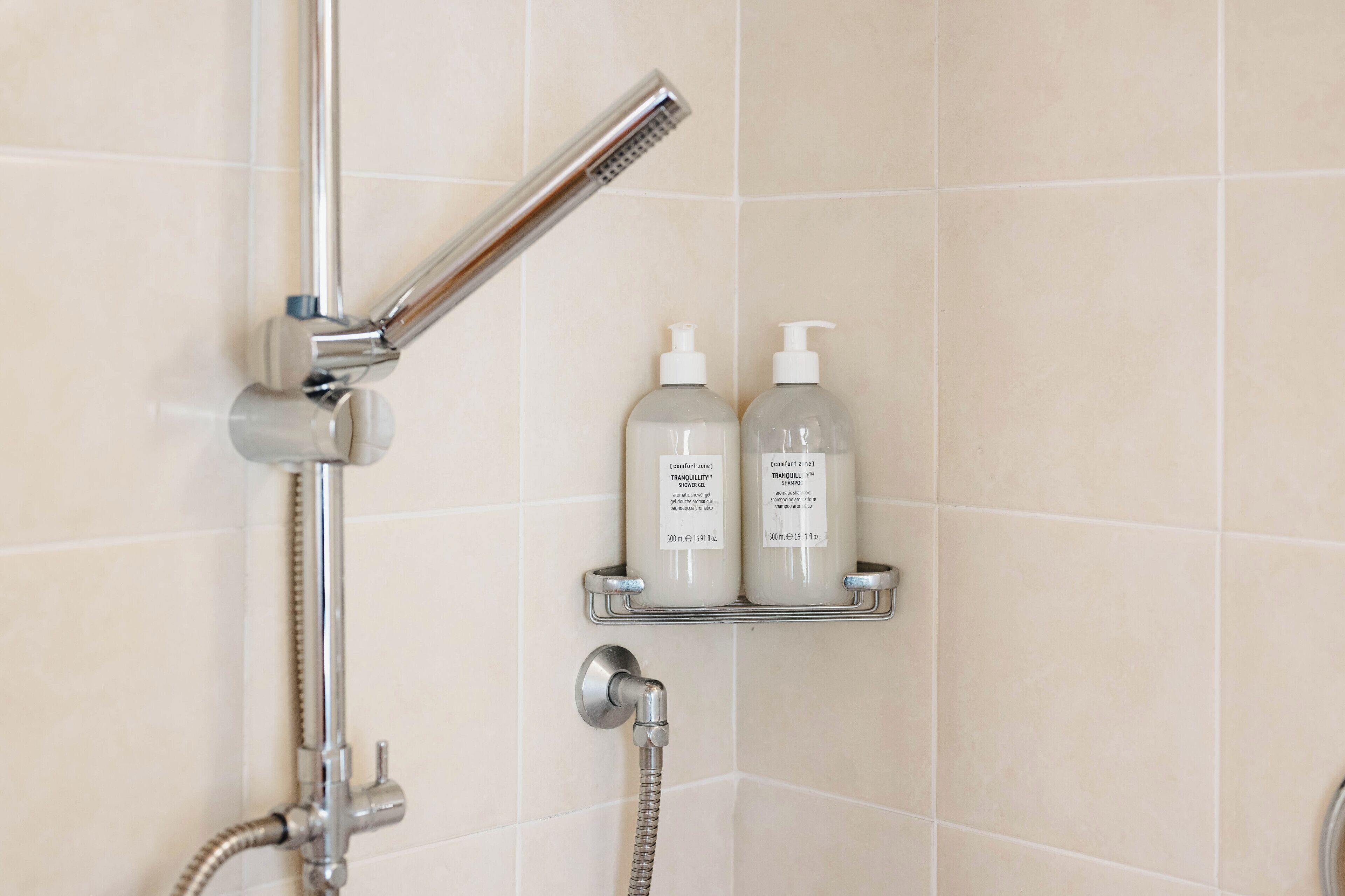 A shower area with a chrome showerhead, a handheld shower attachment, and two bottles of shampoo on a shelf.
