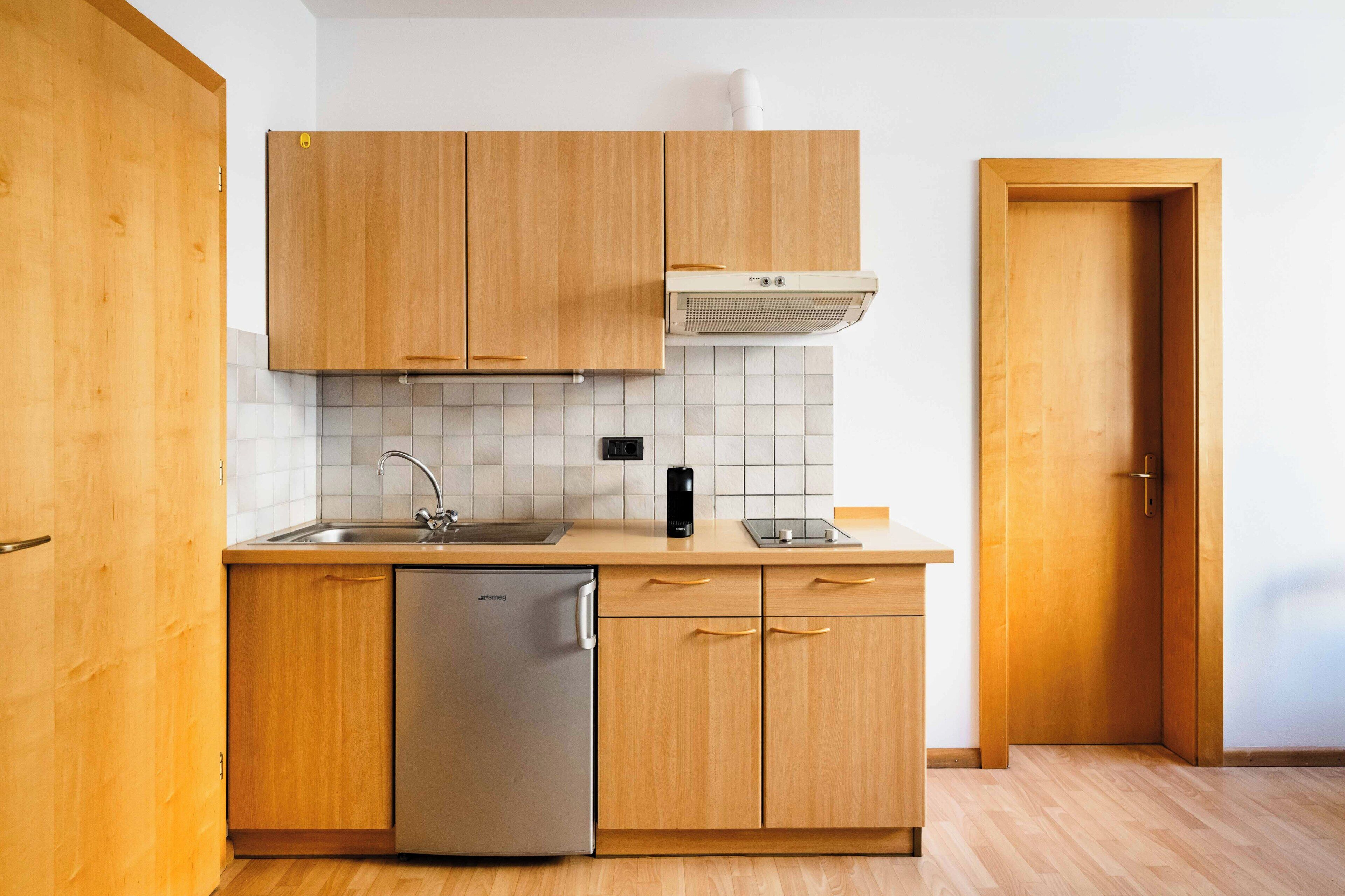 A kitchen with wooden cabinets, a stainless steel dishwasher, a white tiled backsplash, and a wooden door.