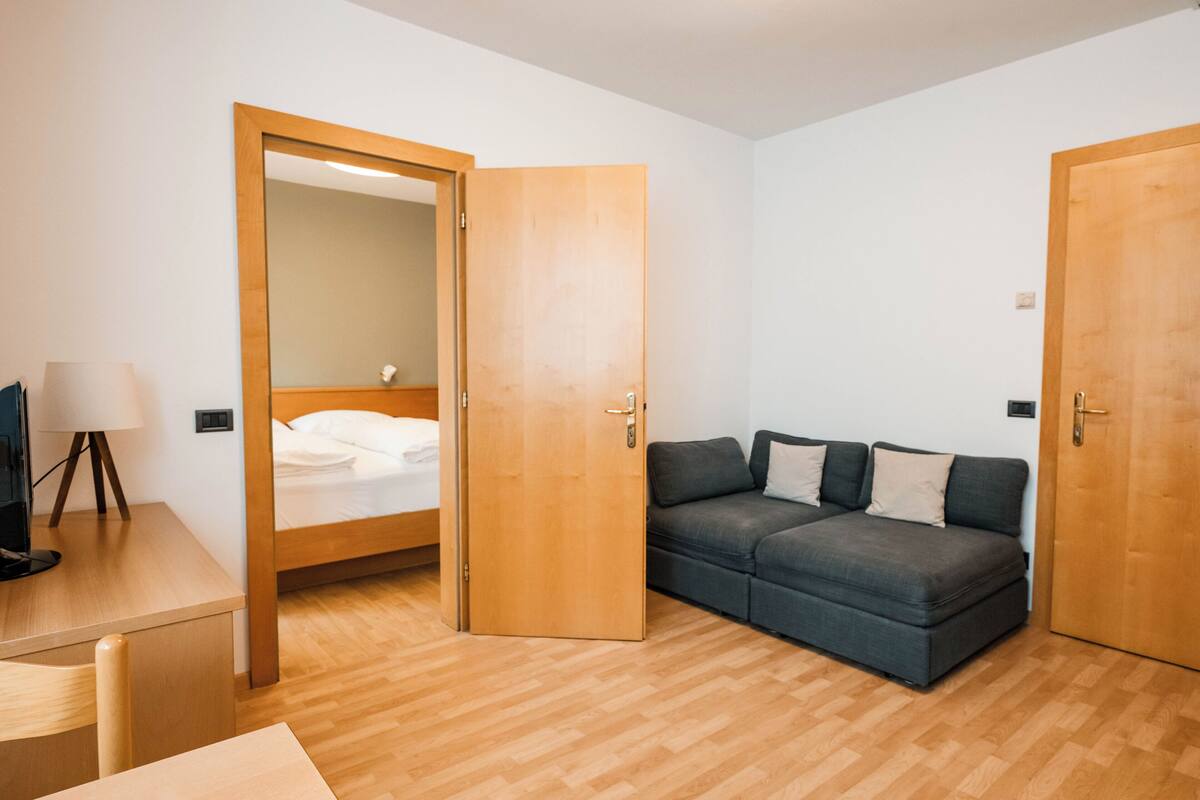A room with a bed, a sofa, a desk with a lamp, and two wooden doors.