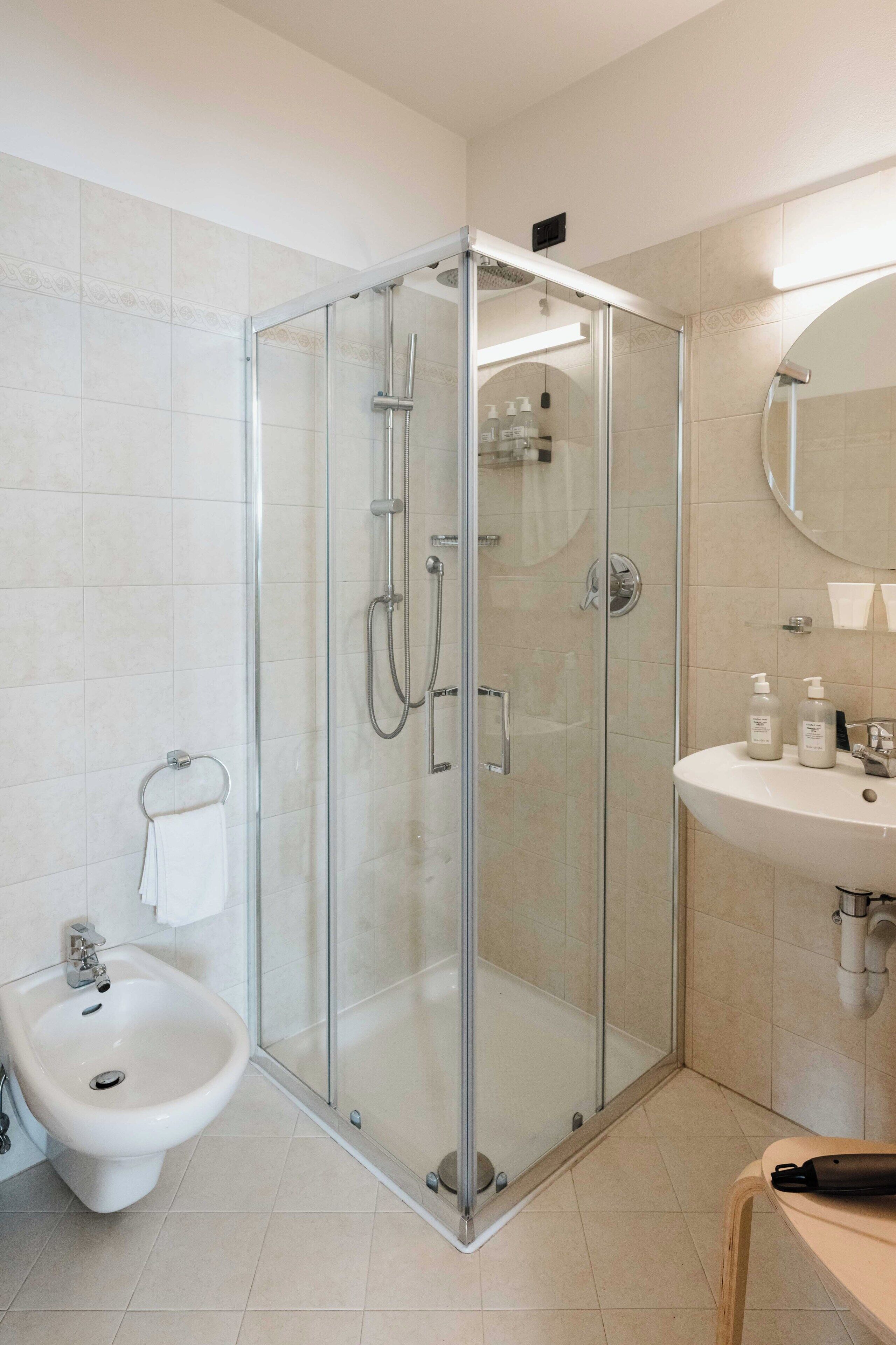 Une salle de bain moderne dotée d’une douche à parois de verre, d’un bidet et d’un lavabo avec des articles de toilette.