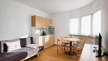 Ein modernes, kompaktes Wohnzimmer mit Sofa, Esstisch, Stühlen, Fernseher und Küchenzeile.
