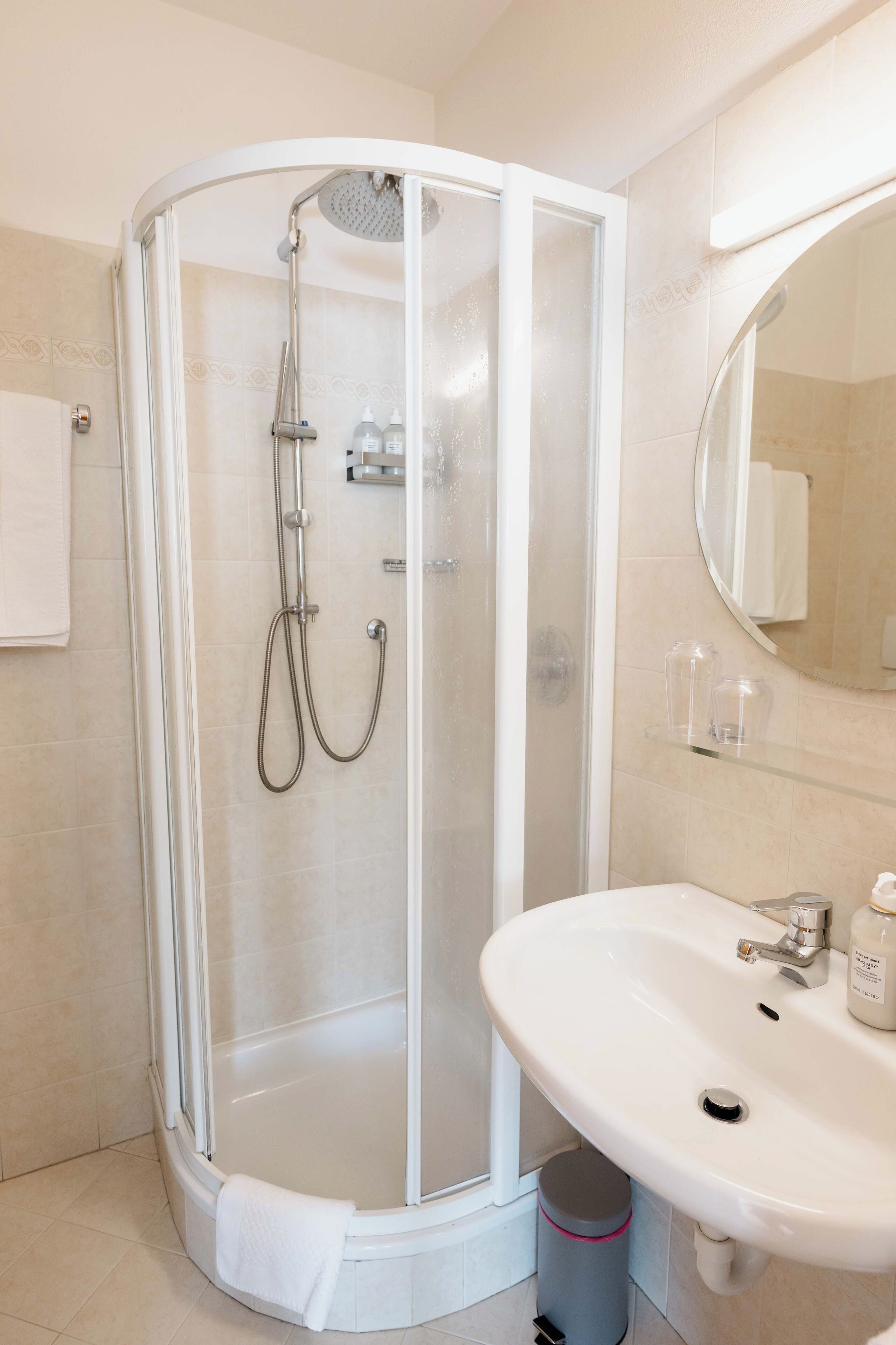 Un baño moderno con ducha de vidrio, un lavamanos blanco y un espejo sobre él.